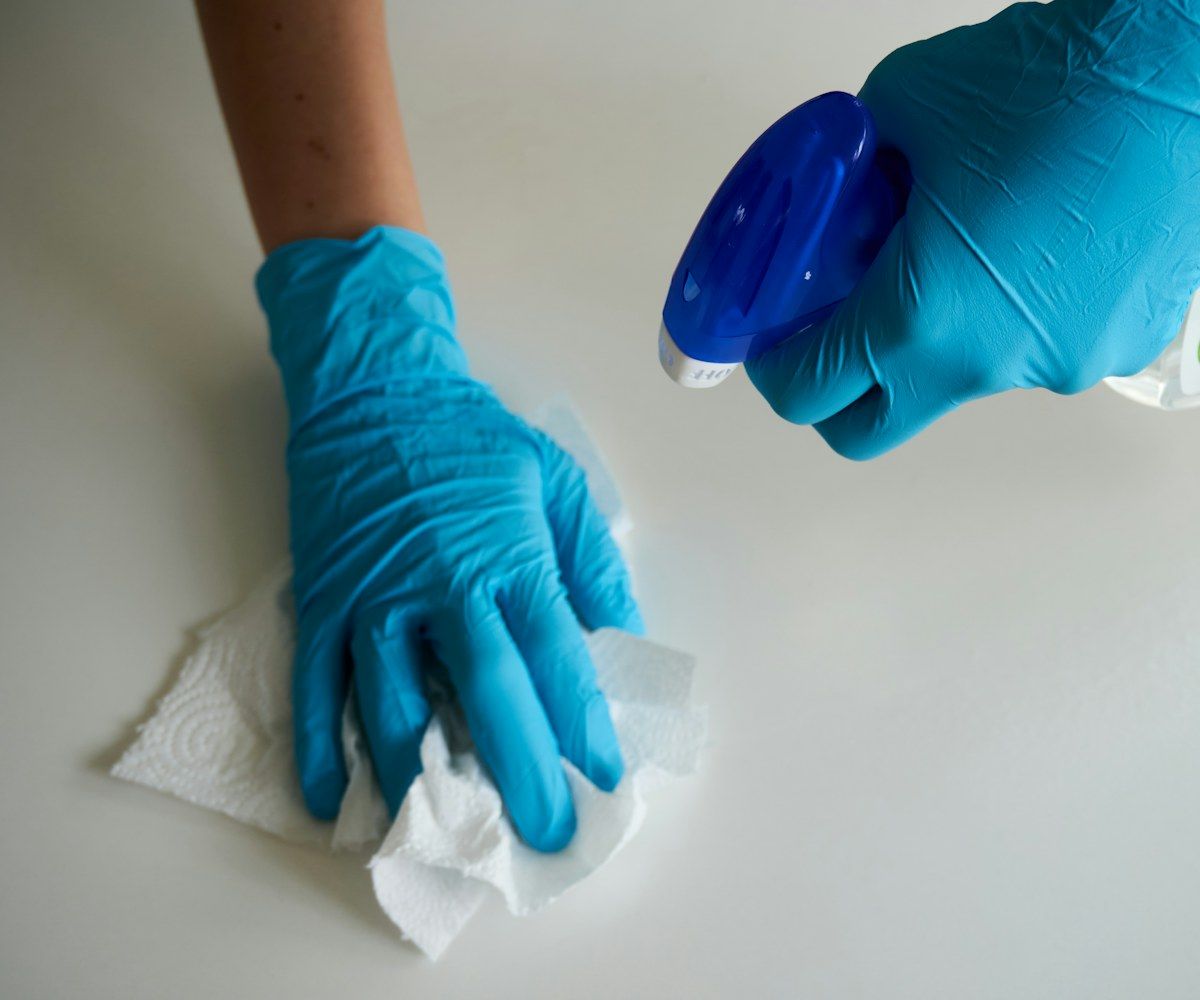 Hände in blauen Handschuhen desinfizieren eine Oberfläche